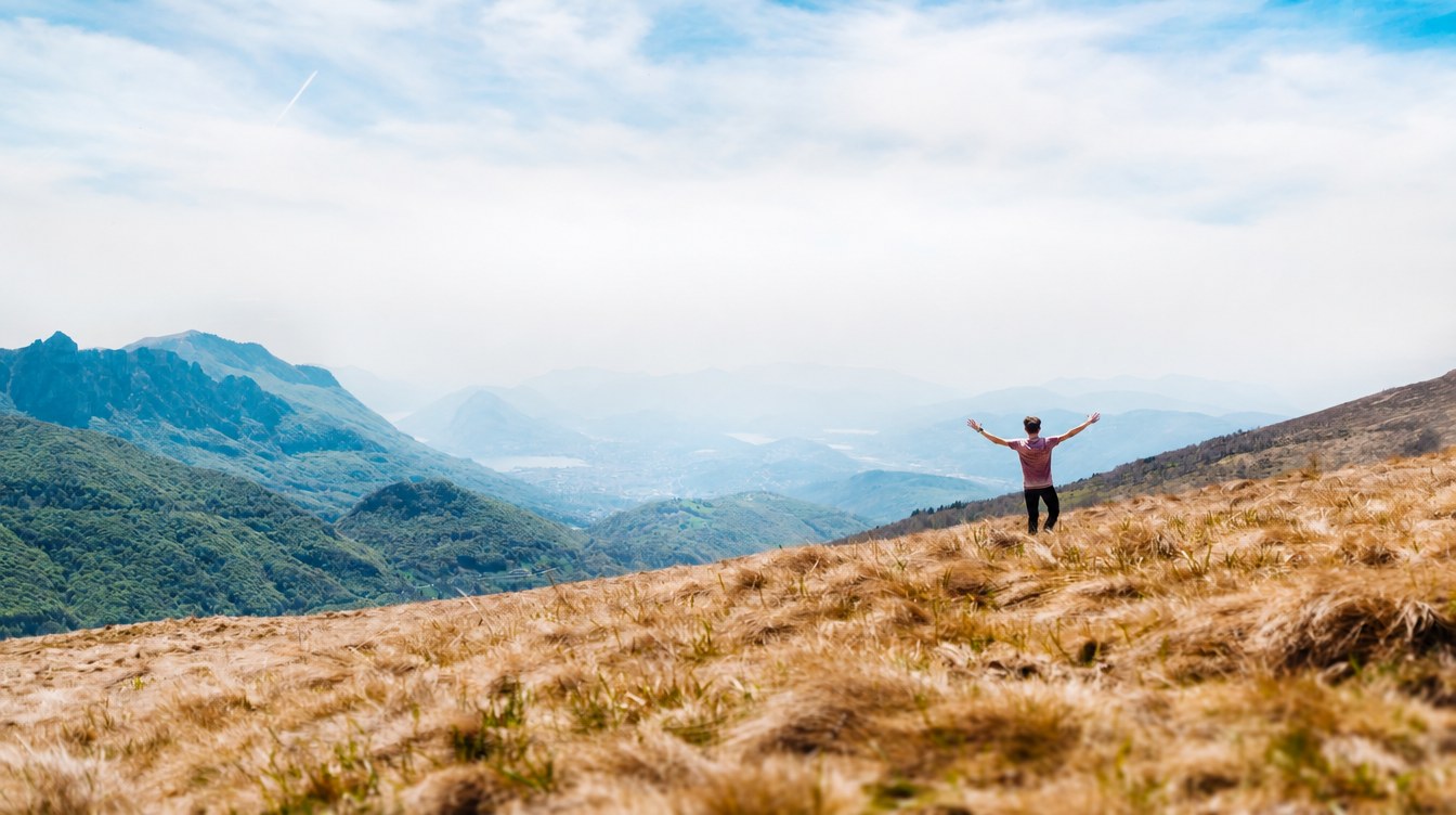 Man with arms raised overlooking a mountain valley — Optimum Health & Performance